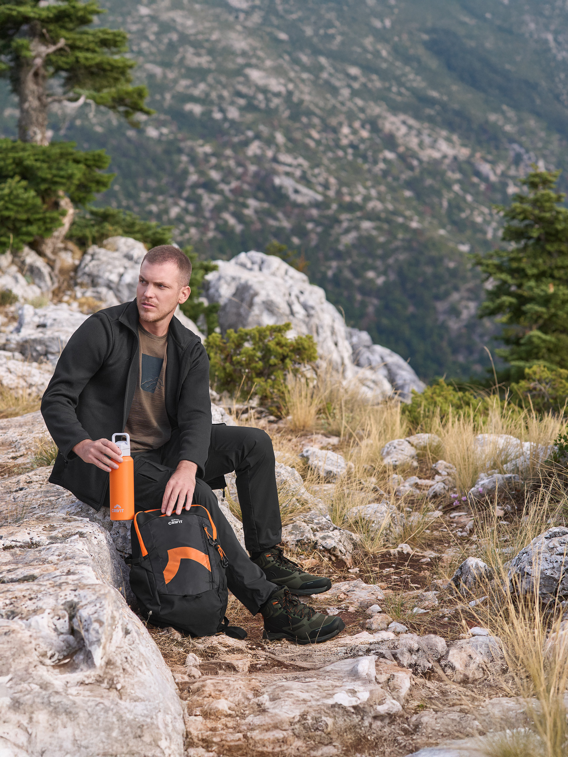 Man in Crivit outdoorjas en -broek, met oranje Crivit waterfles, en Crivit rugzak.
