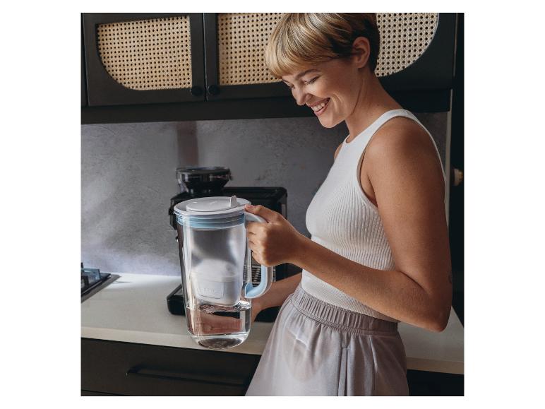 Een vrouw houdt een BRITA glazen waterfilterkan vast in een keuken.