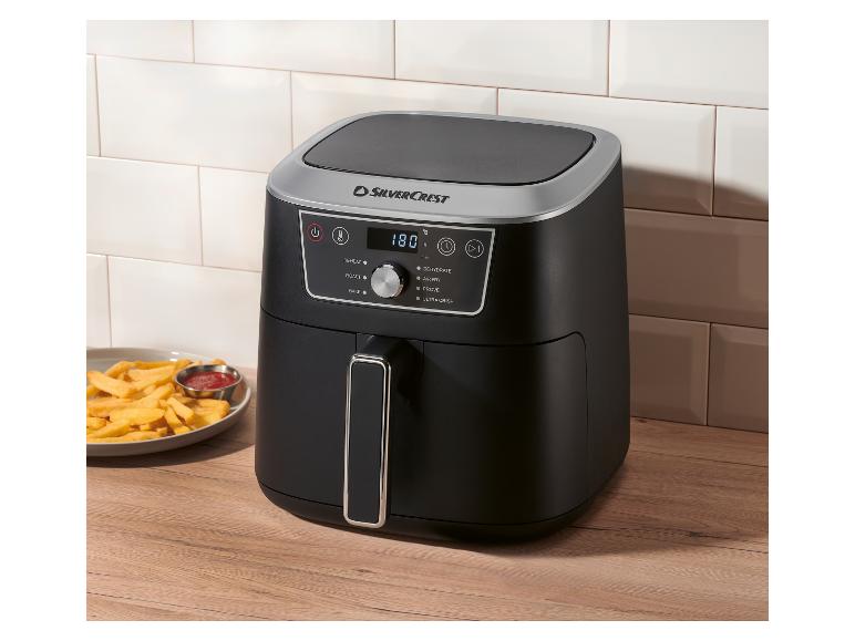 Zwarte airfryer met digitaal display (180°C), naast een bord friet en ketchup.