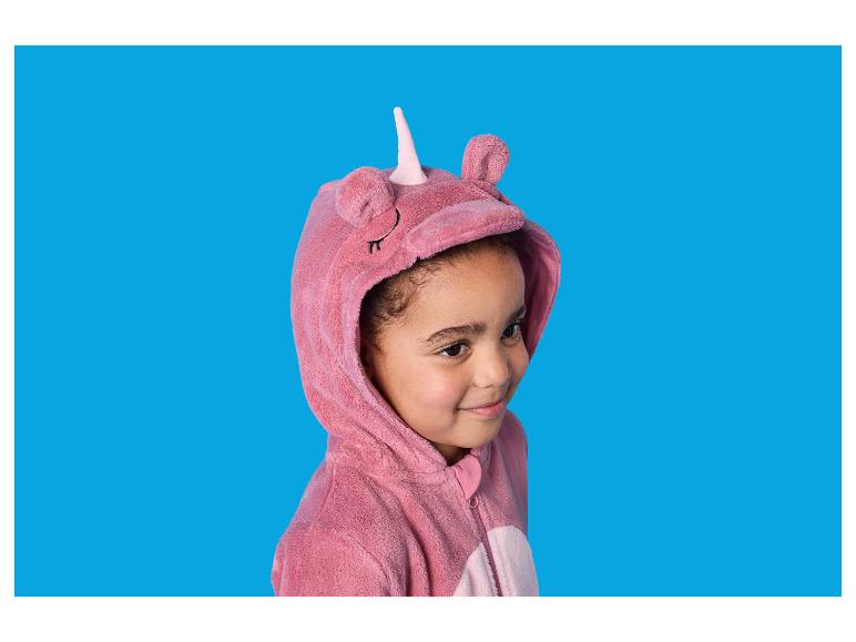 Meisje in een roze eenhoornpyjama, lachend op een blauwe achtergrond.