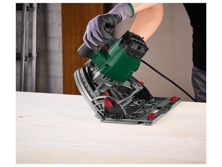 Een groene cirkelzaag met een geleiderail op een houten werkbank.