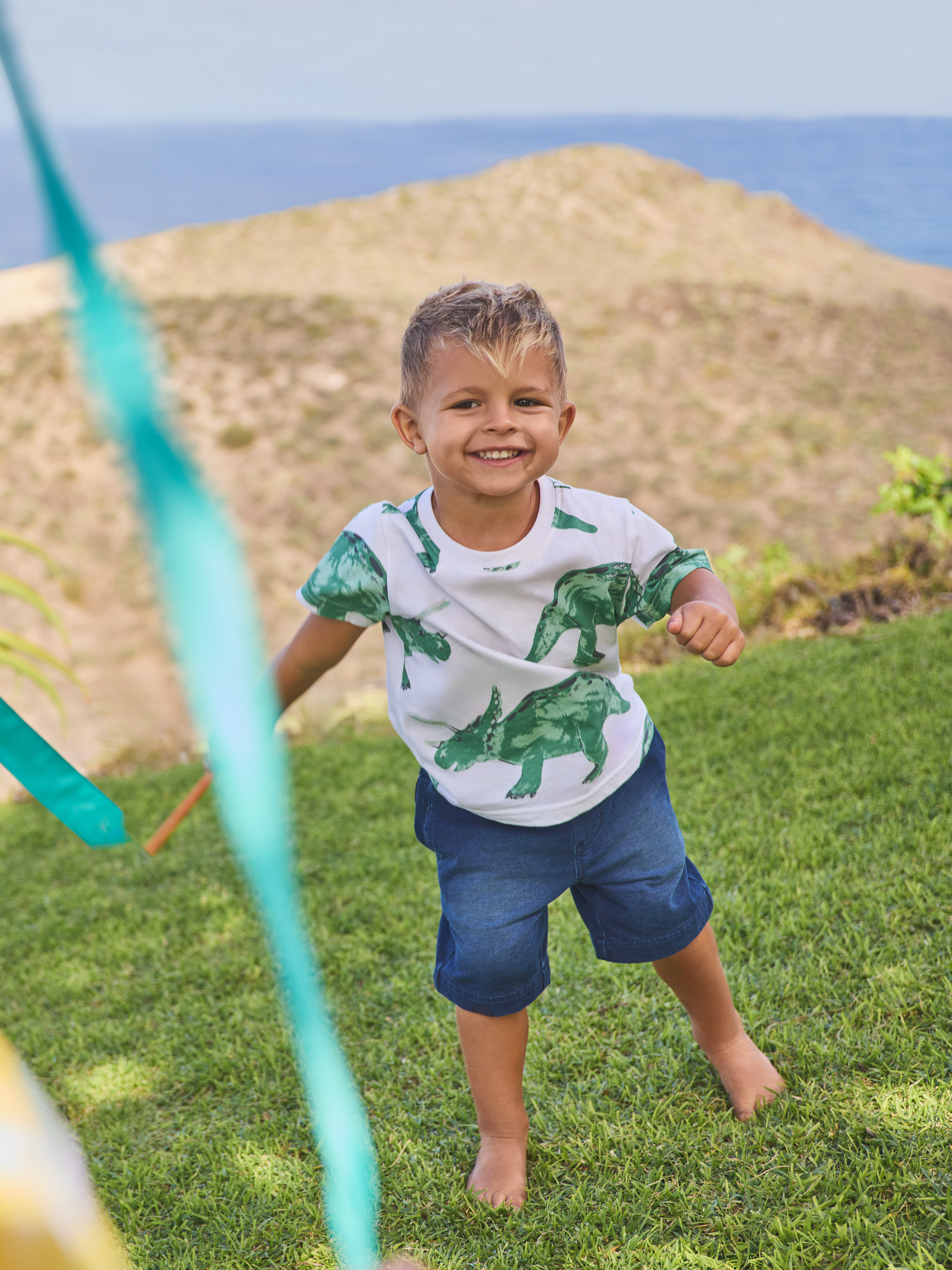 Jongen in dinosaurus T-shirt en spijkerbroek, buiten spelend.