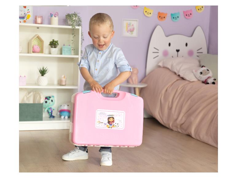 Een jongen houdt een roze Gabby's Dollhouse speelgoedkoffer vast in een kinderkamer.