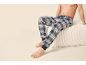 Man met ontbloot bovenlijf in blauw-wit geruite pyjamabroek, zittend op een witte poef.