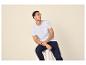 Man in wit T-shirt en blauwe broek zittend op een kruk.
