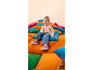 Lachend meisje in jeans en roze sneakers zit op kleurrijke kussens.