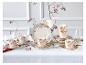 Bloemig servies met kopjes, schotels en borden op een wit tafelkleed.