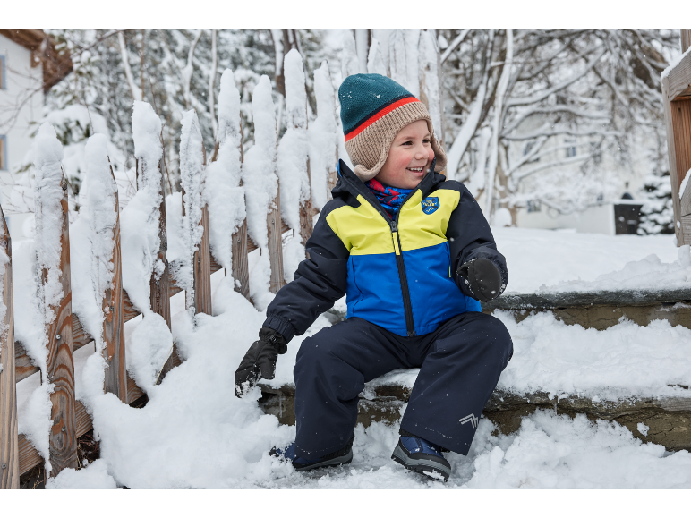 Lachend kind in ski-jas en sneeuwbroek zit op besneeuwde treden.