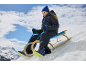 Meisje in blauw skipak en muts, zittend op een houten slee in de sneeuw.