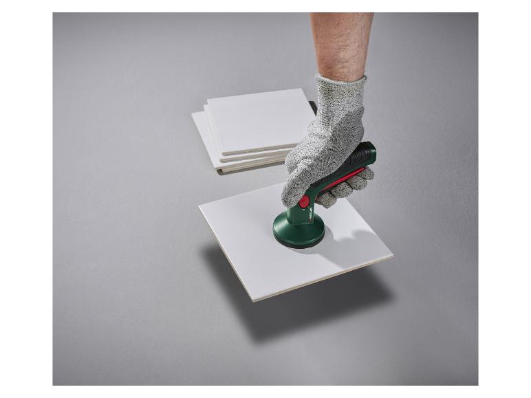 Hand in werkhandschoen gebruikt een zuignap op een witte keramische tegel.