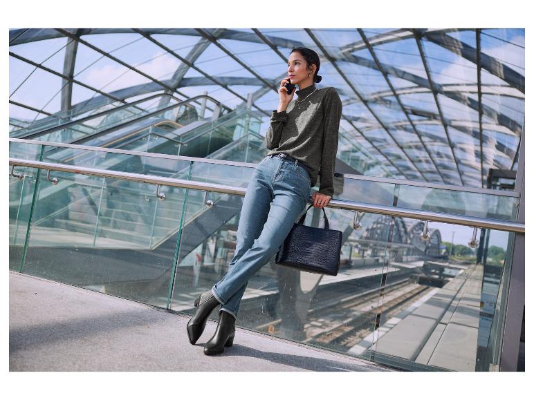 Een vrouw draagt een grijze trui, blauwe jeans en zwarte laarzen.