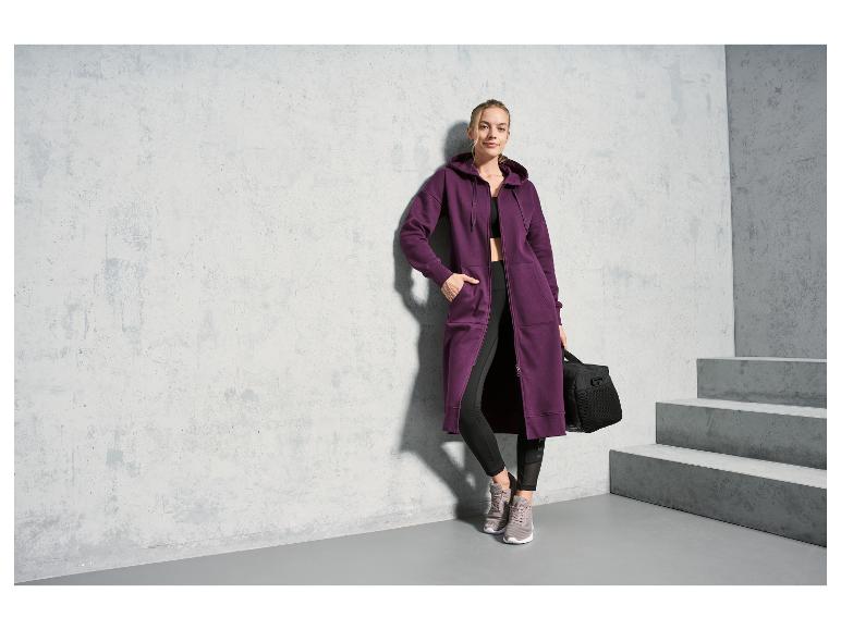 Een vrouw in een paarse hoodie en zwarte leggings, met een sporttas.