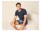 Man in een marineblauw T-shirt en geruite shorts, zittend op een beige bank.