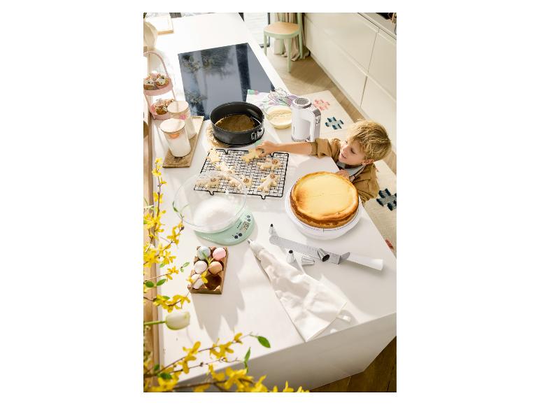Kind bakt koekjes en cheesecake met keukengerei en paasdecoraties.