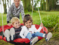 Twee kinderen op een rode schommel in de tuin.