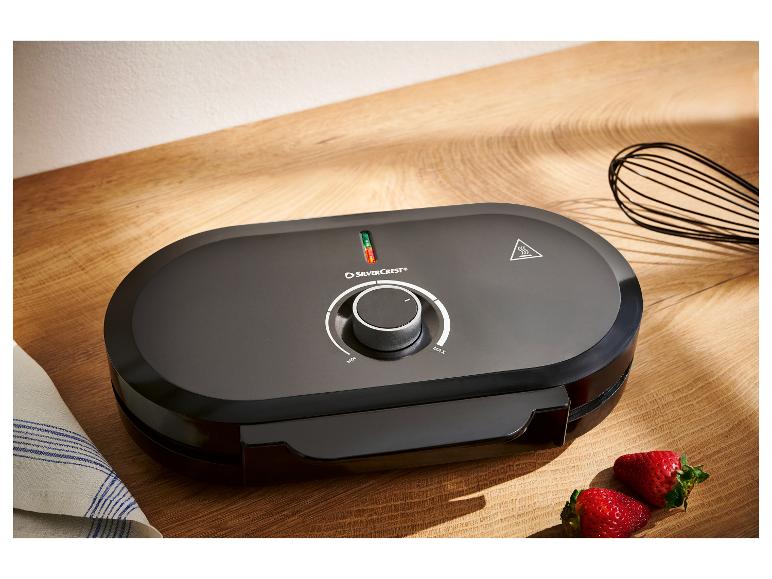 Zwart SilverCrest wafelijzer op houten ondergrond met aardbeien en garde.