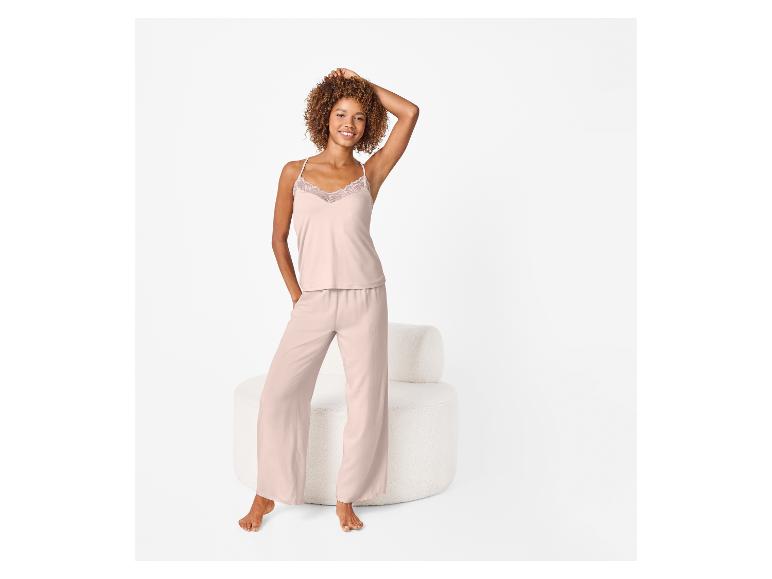 Vrouw draagt roze pyjama met kanten top, staand naast een witte fauteuil.