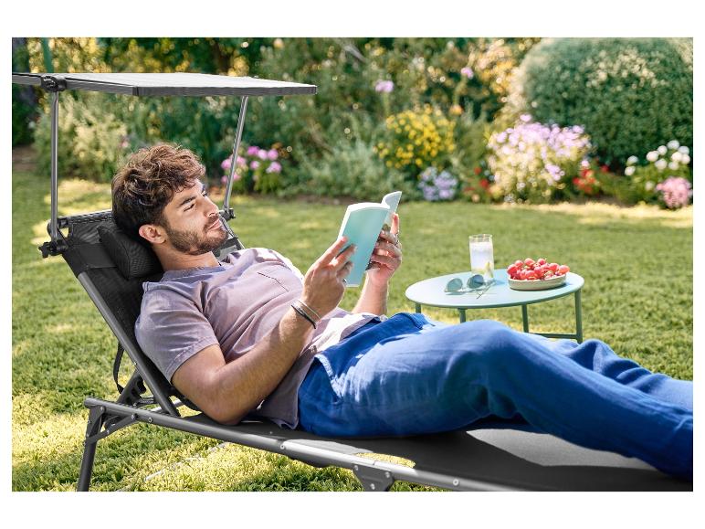 Man ontspant op een tuinstoel met zonnescherm, leest een boek in de tuin.