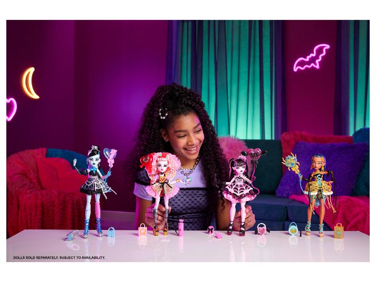 Een lachend meisje houdt Monster High-poppen vast, met andere poppen en accessoires op een tafel.
