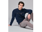Man in donkerblauwe trui met tekst en grijze broek, zittend tegen een grijze achtergrond.