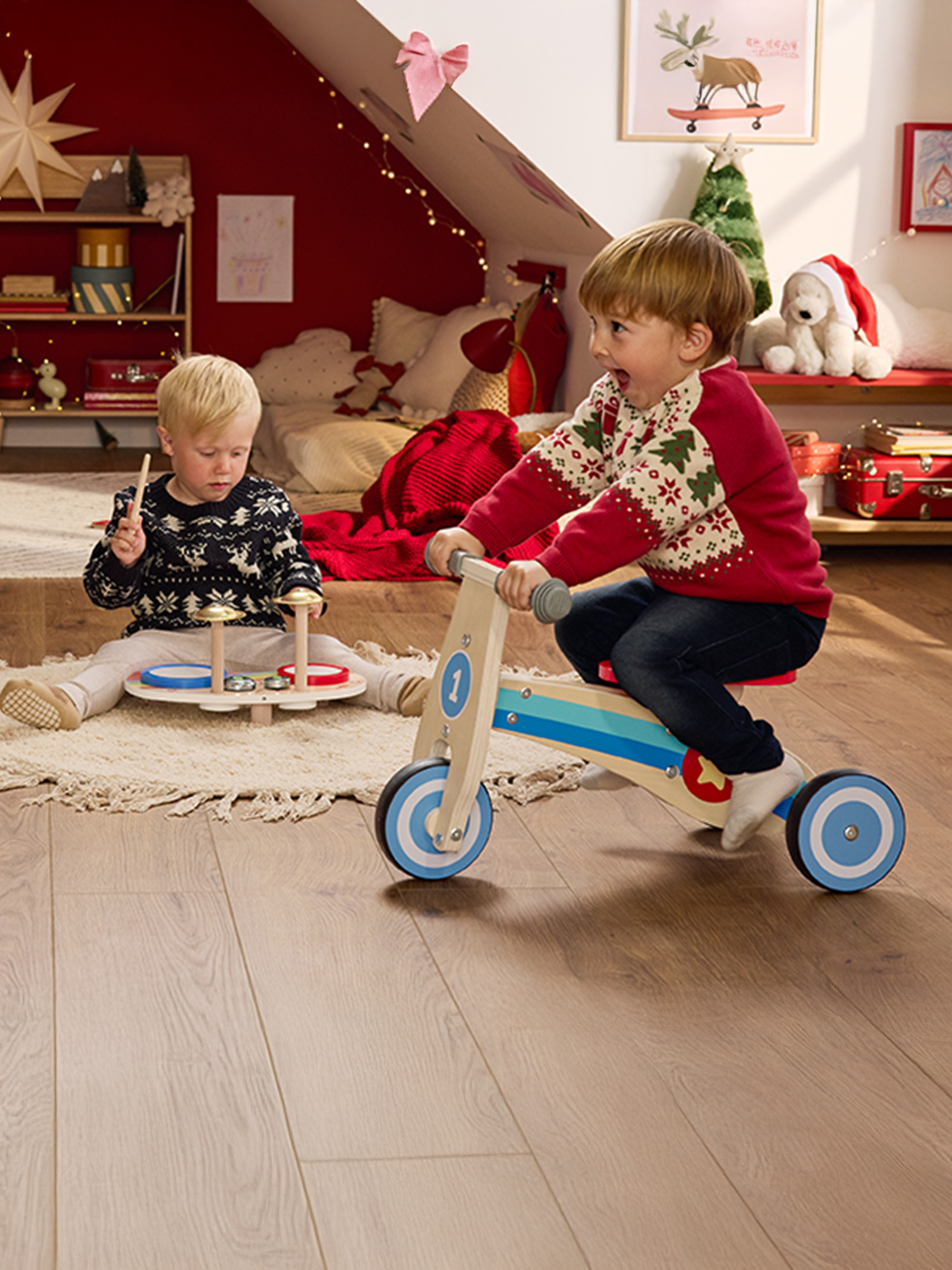 Twee kinderen spelen met houten speelgoed in een kerstversierde kamer.