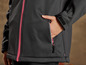 Een zwarte softshell jas met roze rits en een zak met rits.