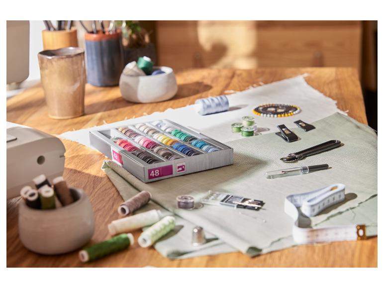 Naaibenodigdheden op een houten tafel: garenklosjes, naalden, meetlint en andere accessoires.