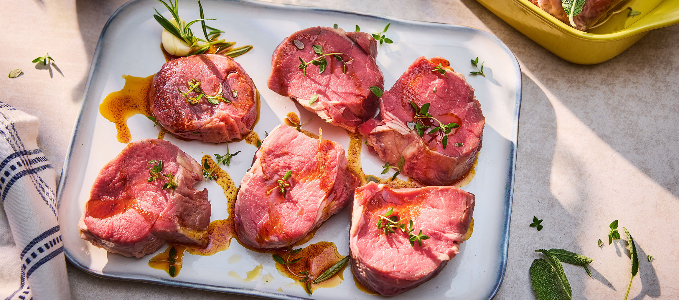Verse rundersteaks met kruiden en olie op een wit bord.