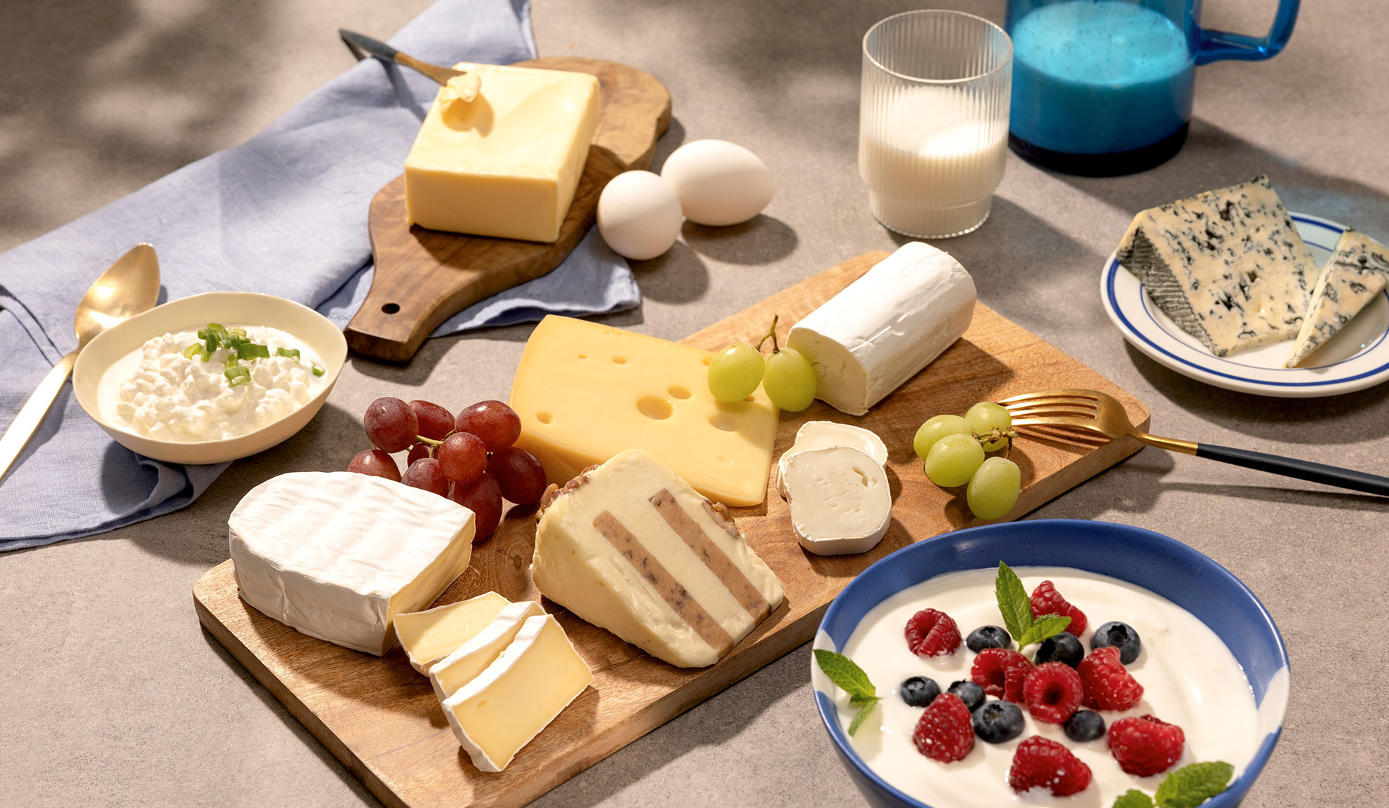 Een verscheidenheid aan kazen, druiven en zuivelproducten zoals hüttenkäse, melk en yoghurt met bessen.