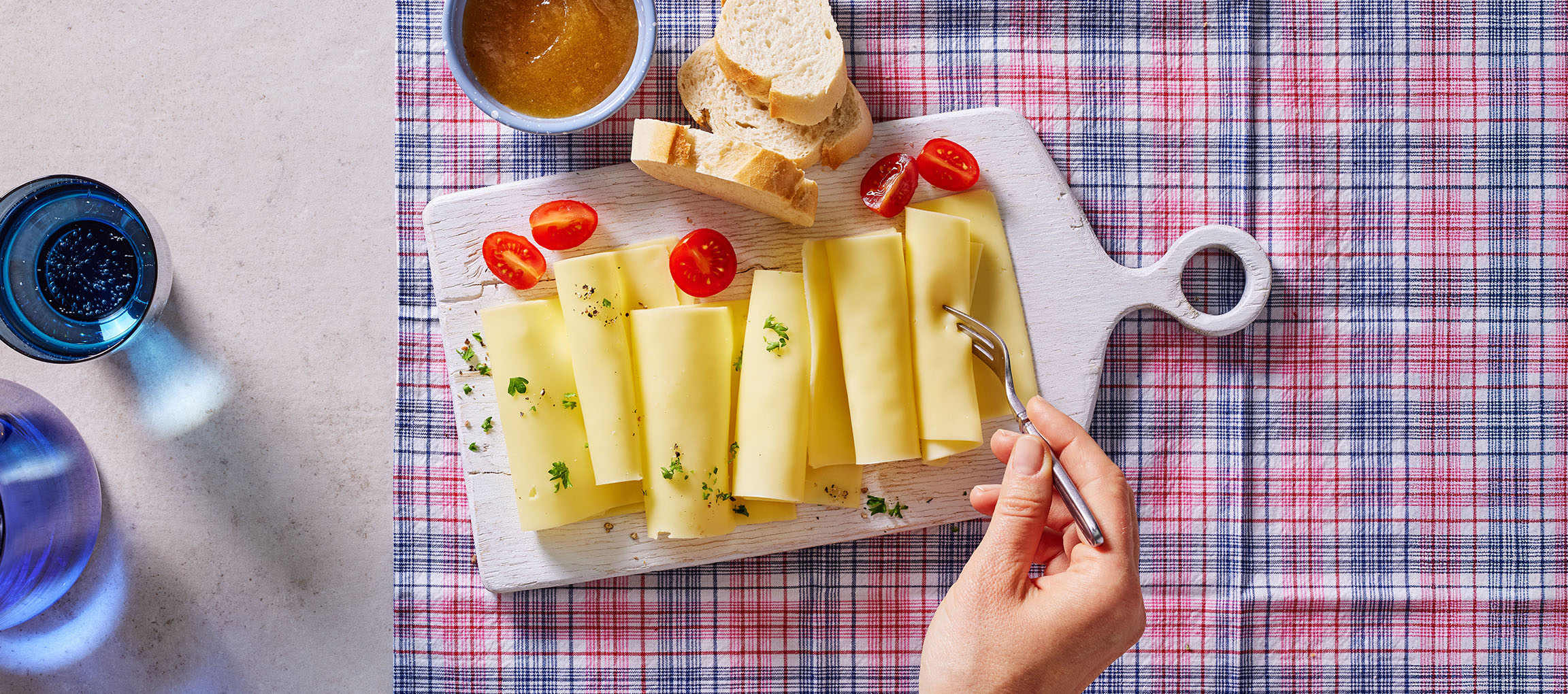 Kaasplakjes met cherrytomaten, brood en jam op een geruite tafelkleed.