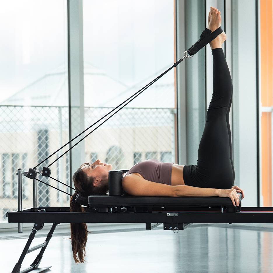 Vrouw doet beenoefening op een pilates reformer apparaat.