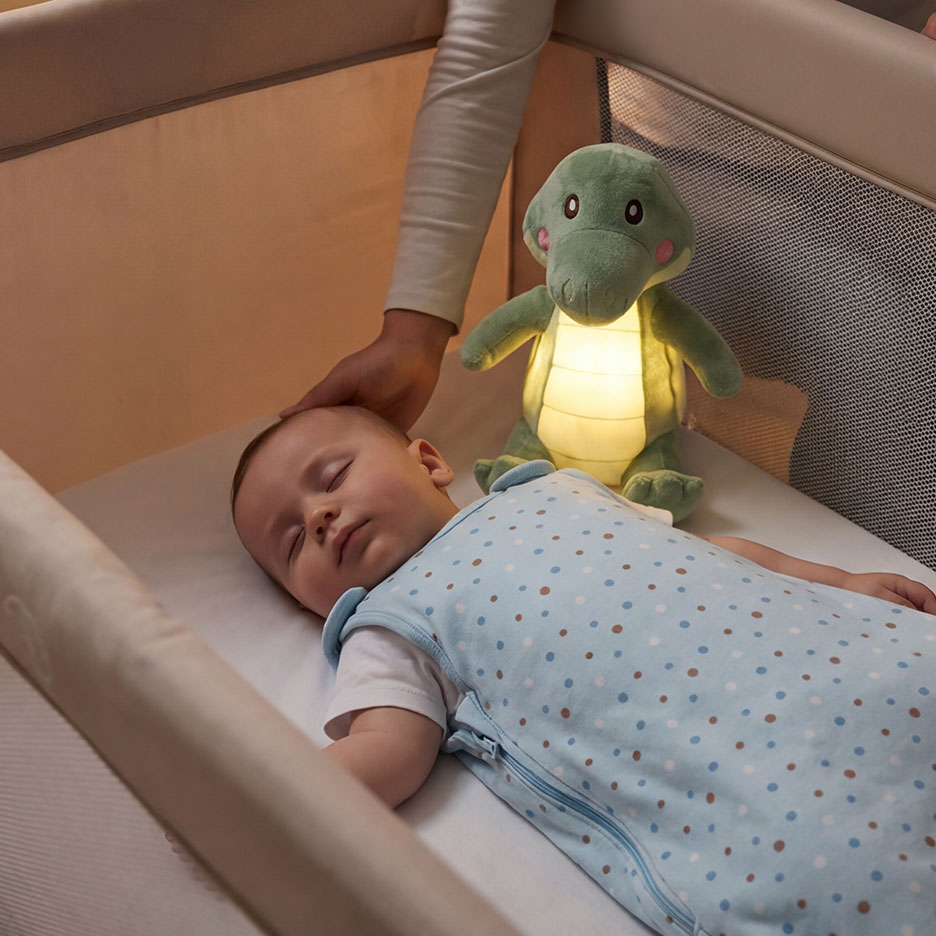 Baby slaapt in wieg met gloeiend krokodil nachtlampje en een hand die zachtjes het hoofd aanraakt.
