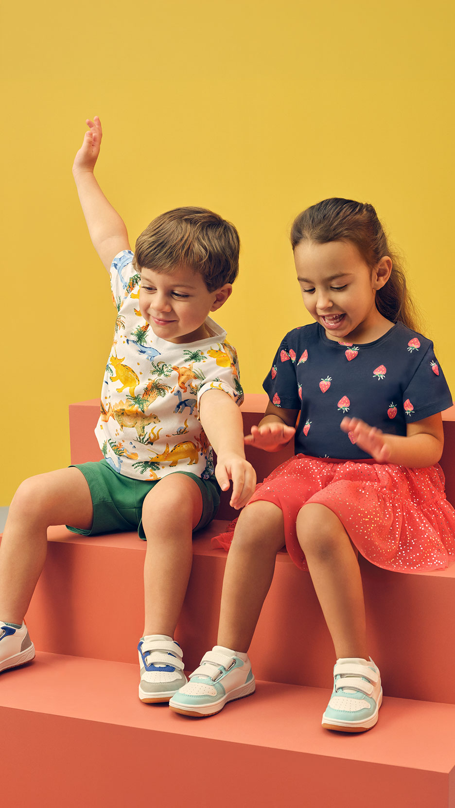 Twee kinderen zitten op treden, jongen in dinosaurus-T-shirt, meisje in aardbeien-T-shirt.