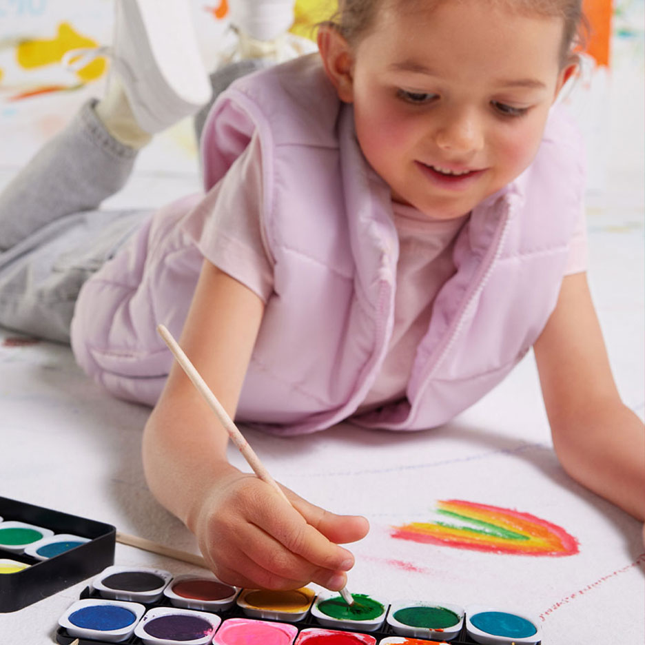 Meisje schildert regenboog met waterverf en kwast op papier.