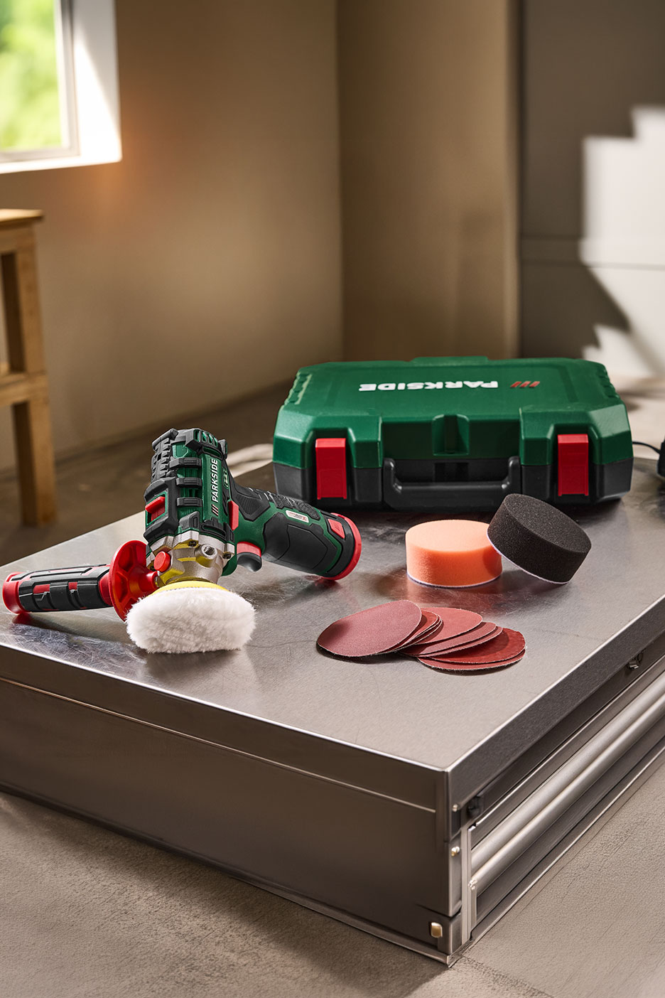 Draadloze polijstmachine met polijst- en schuuraccessoires op een metalen tafel.