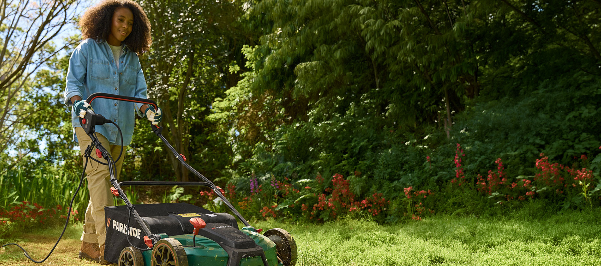 Vrouw in een tuin gebruikt een elektrische grasmaaier om gras te maaien.