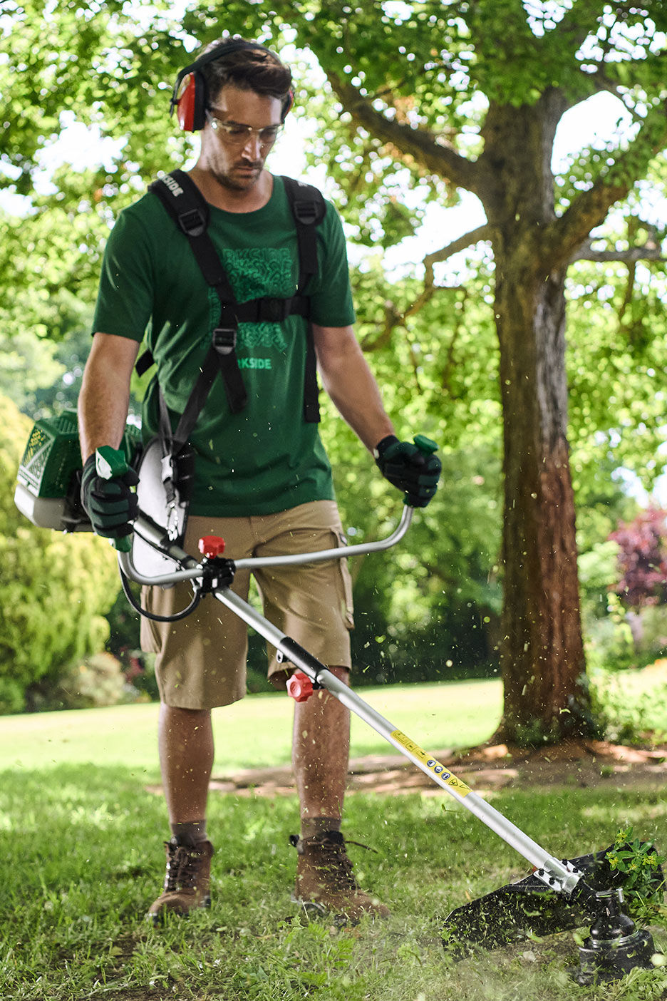 Man gebruikt bosmaaier met harnas, gehoorbescherming en veiligheidsbril in een tuin.