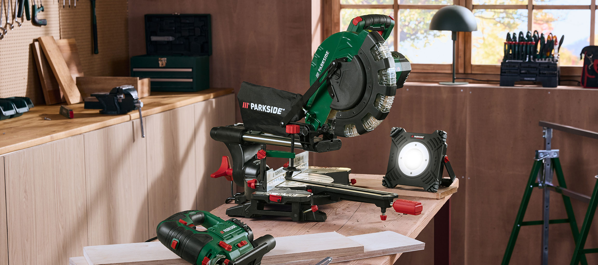 Werkplaats met afkortzaag, werkplaatslamp en ander gereedschap op een houten werkbank.