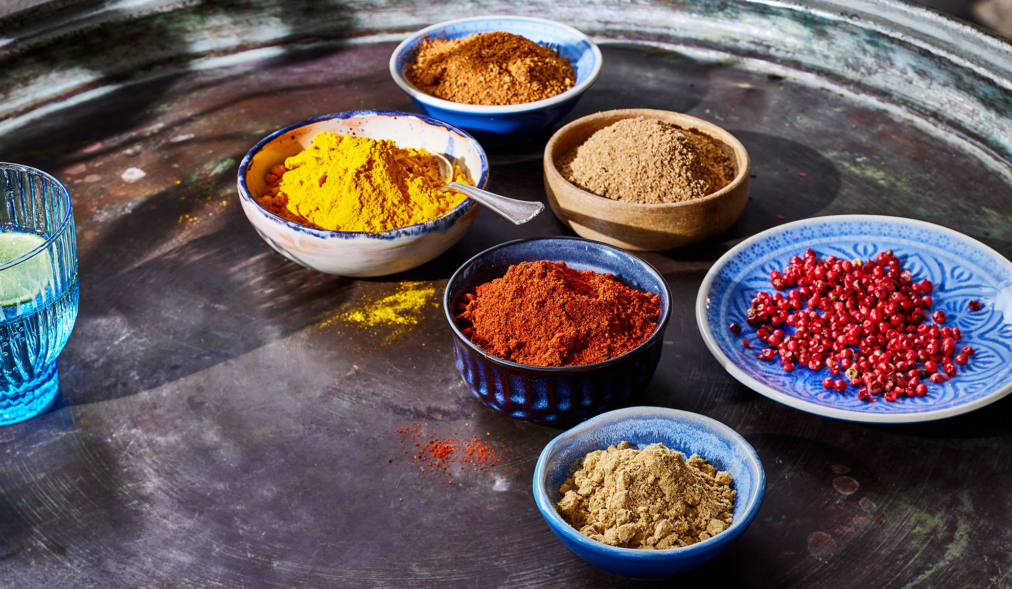 Diverse kruiden in kommen: kurkuma, paprika, peper en andere op een metalen dienblad.