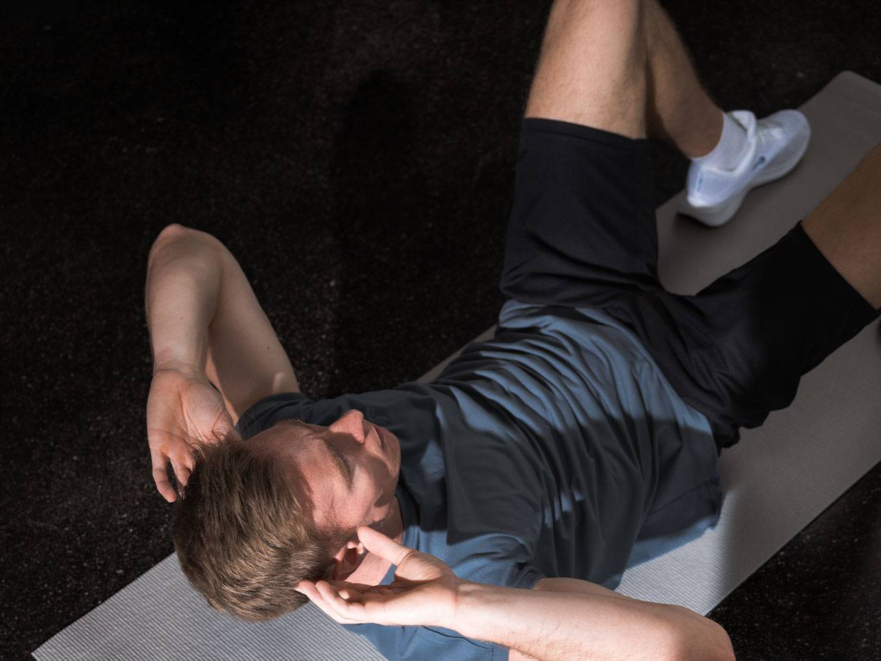 Man in blauw T-shirt en zwarte korte broek doet crunches op een yogamat.