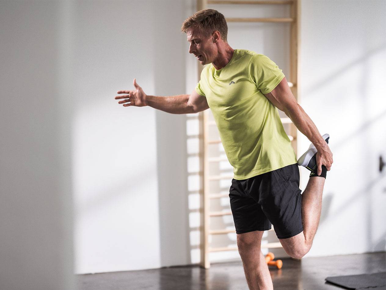 Man rekt in zwarte korte broek en een limoengroen T-shirt in een sportschool.