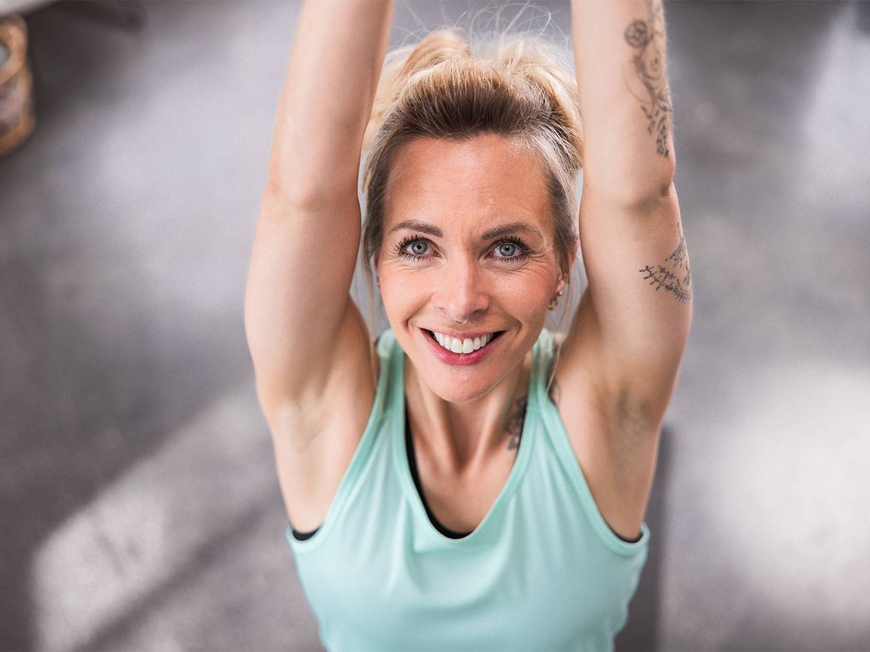 Blonde vrouw in een lichtblauwe tanktop lachend naar de camera.