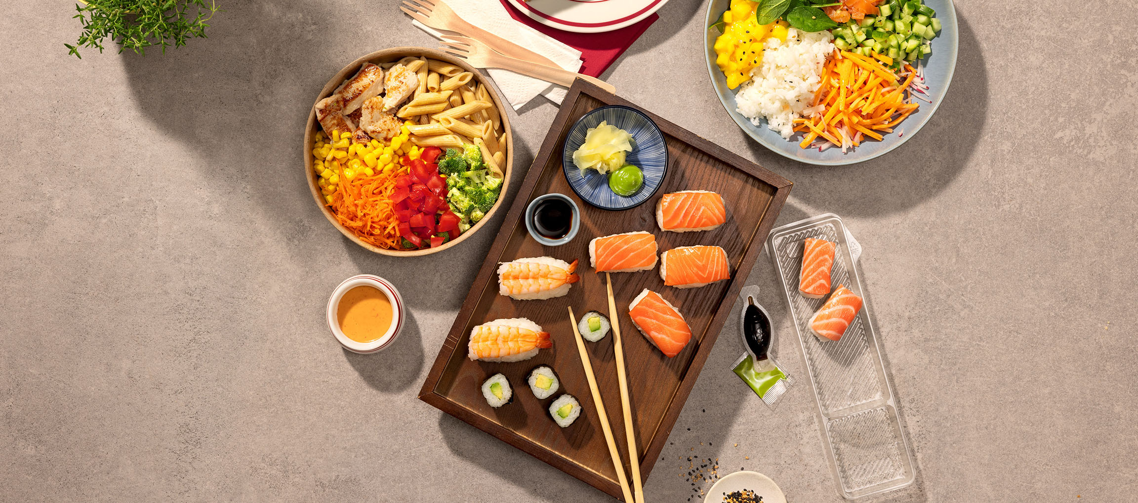 Diverse gerechten: pasta- en kipbowl, sushi en een pokébowl op een tafel.
