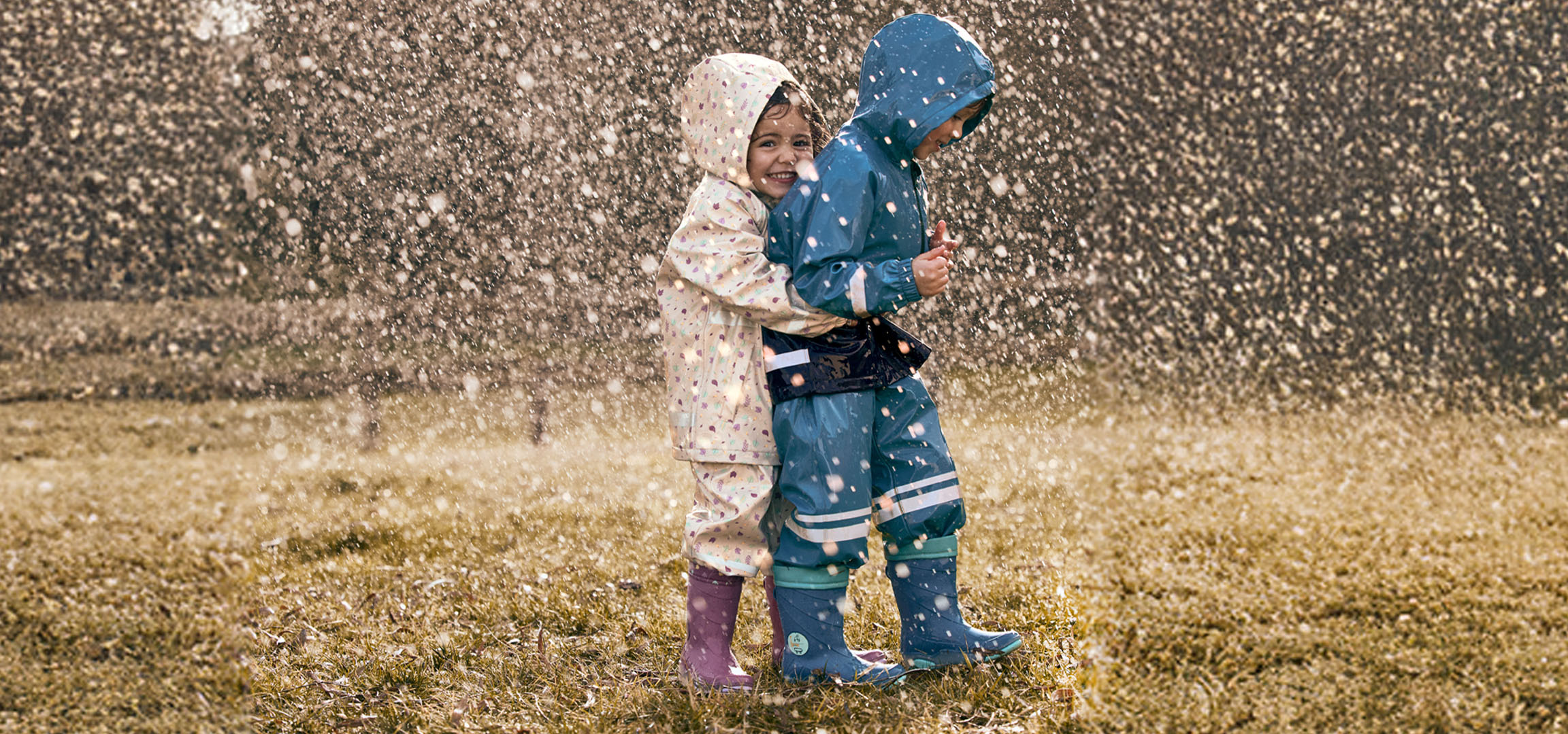 Twee kinderen in regenpakken en regenlaarzen spelen in de regen.