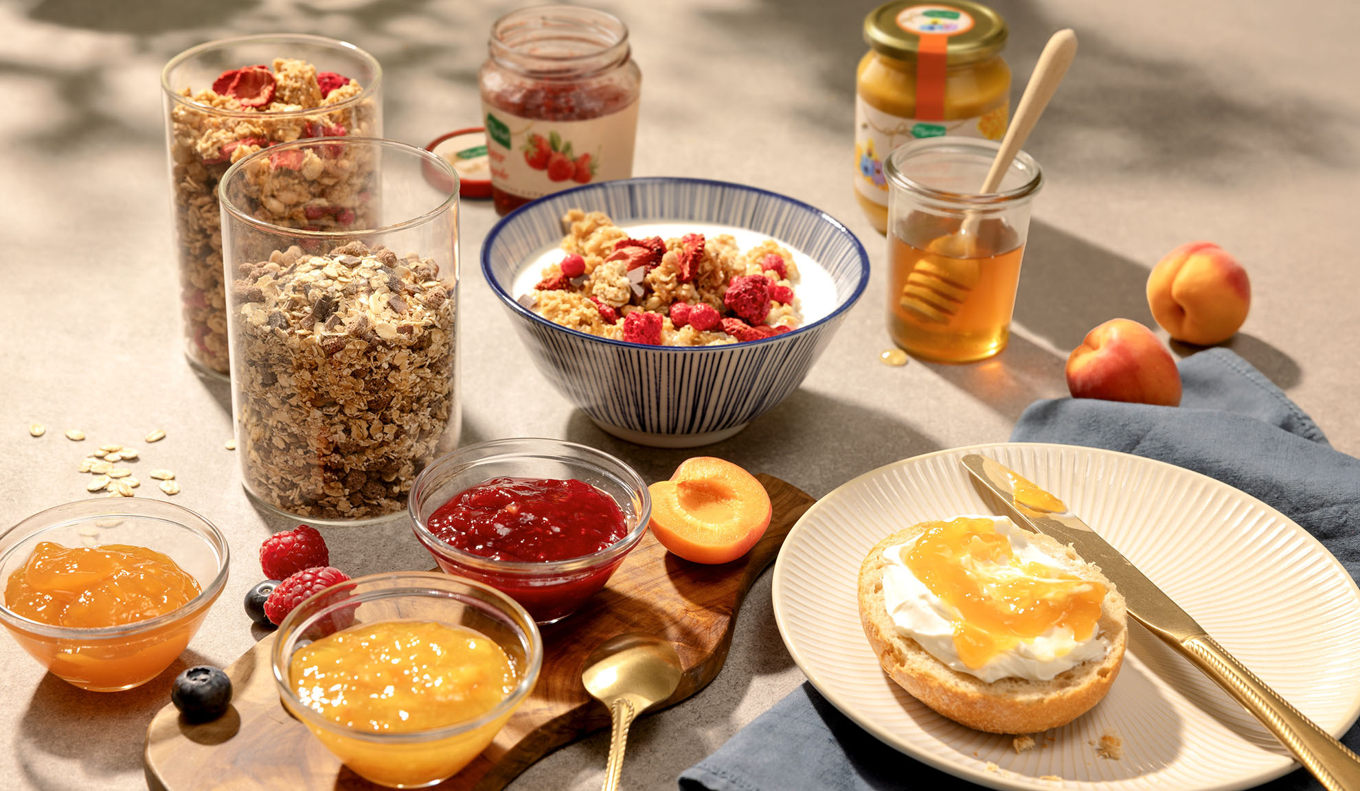 Ontbijt met granola, yoghurt, honing, jam en vers fruit op een zonnige tafel.
