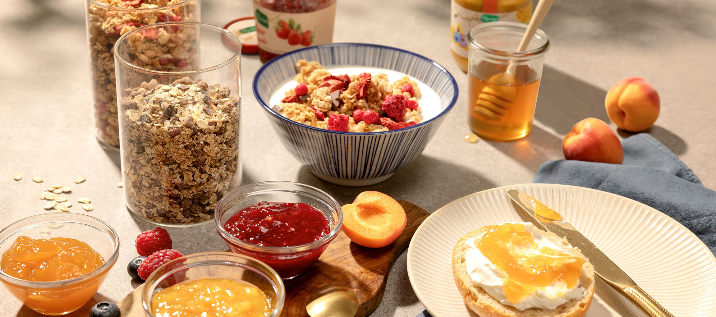 Ontbijt met granola, melk, honing, jam en een broodje met roomkaas.