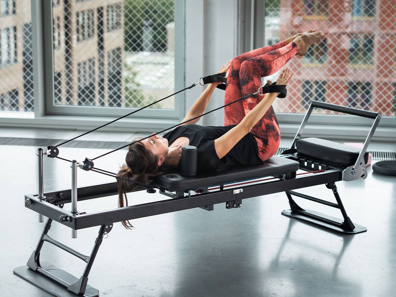 Vrouw doet Pilates op een reformer in een rode yogalegging.