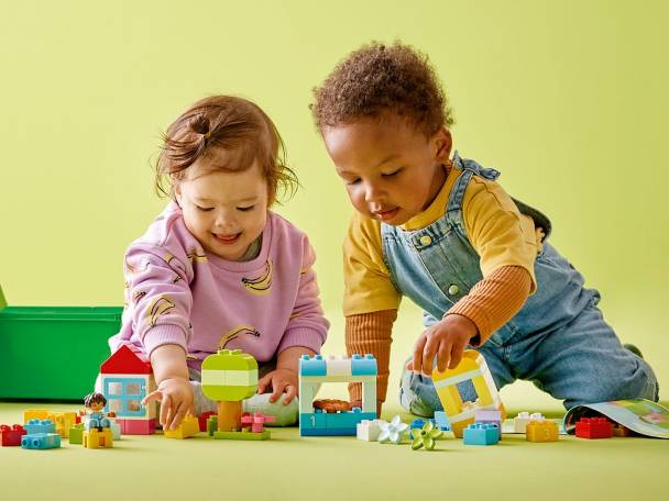 Twee baby's spelen met kleurrijke LEGO DUPLO blokken op een groene achtergrond.
