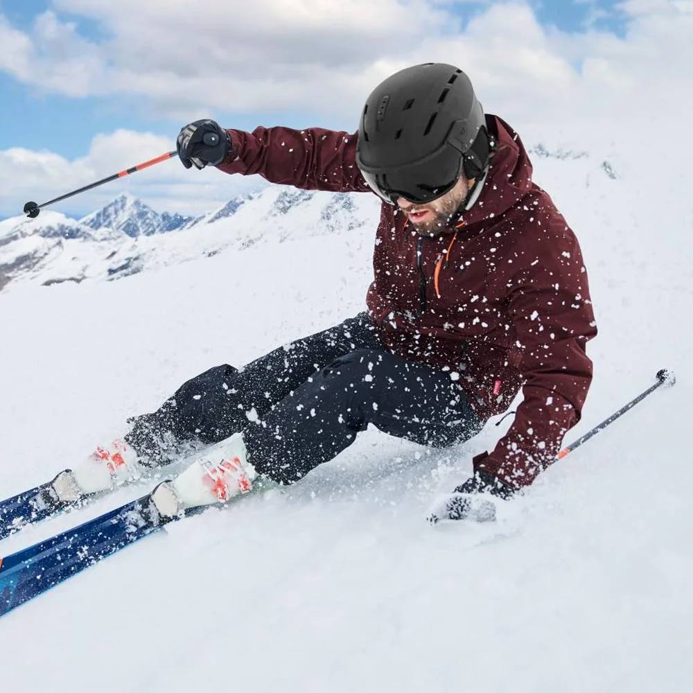 Man in een bordeauxrode ski-jas en zwarte broek skiet op een besneeuwde berghelling.