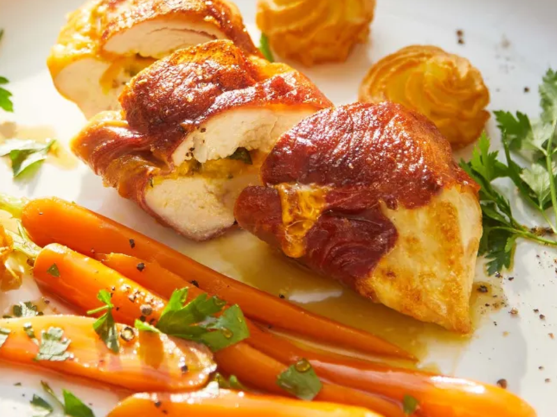 Gevulde kipfilet omwikkeld met spek, geserveerd met worteltjes en aardappelkroketjes.